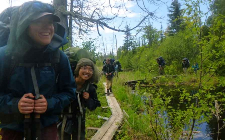 a group of outward bound students smile while hiking on an elevated wood trail through a marsh area